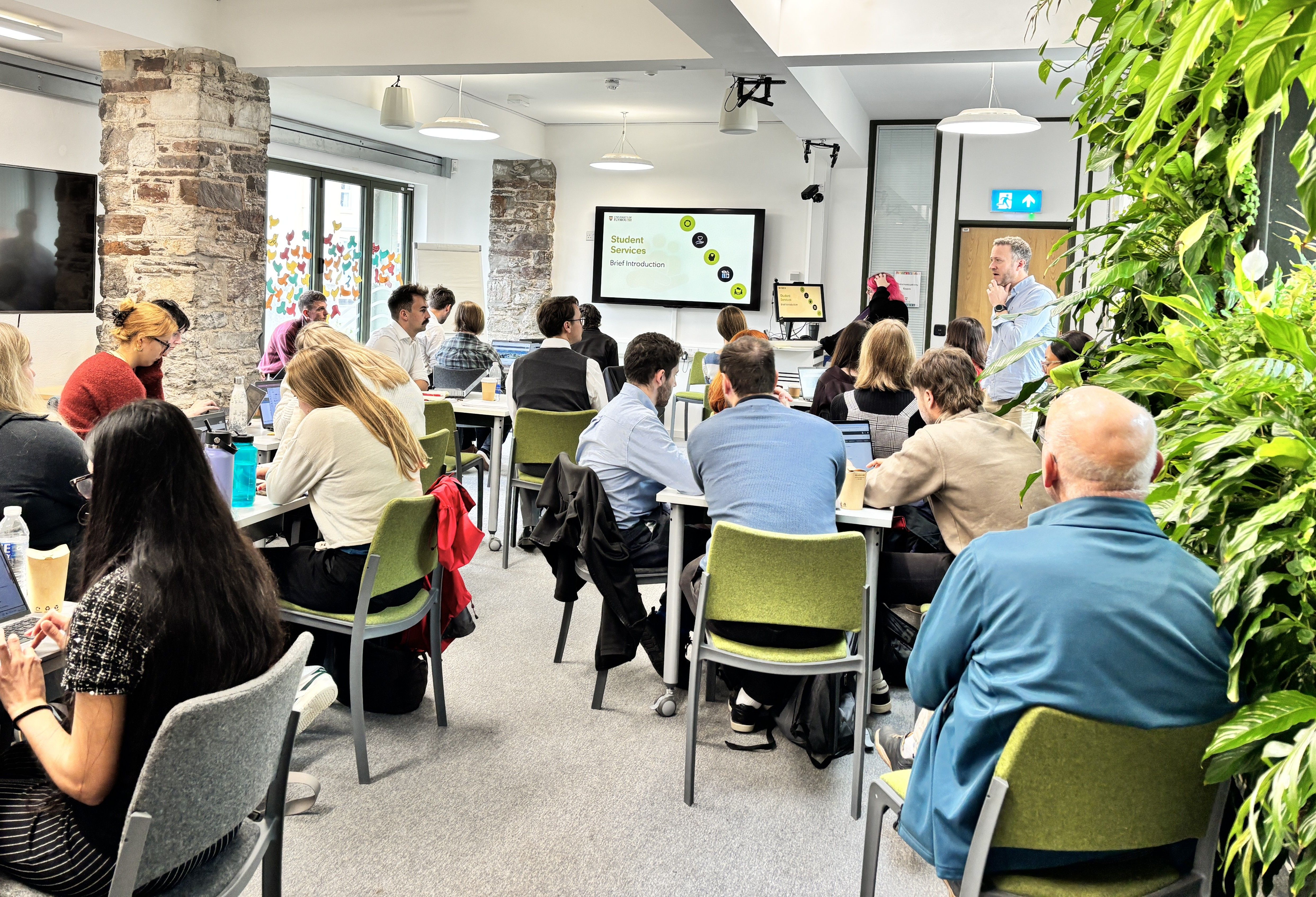 Participants seated at tables during an introductory classroom session, with a presentation displayed on a screen and a speaker addressing the room as part of the Foundation Operational Meteorology Programme.