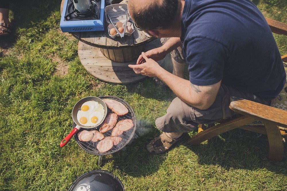 cooking a breakfast of fried eggs and bacon over a camping stove
