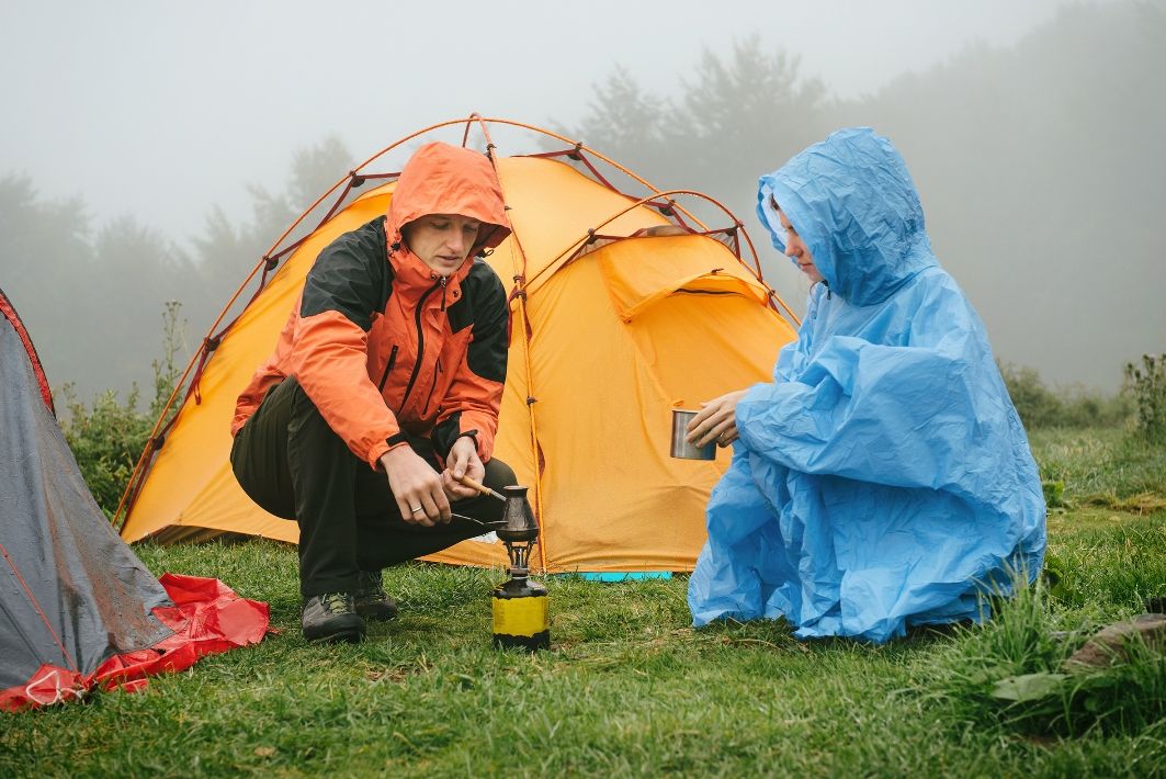 Two people camping in the rain. One wearing a rain coat and the other a rain poncho