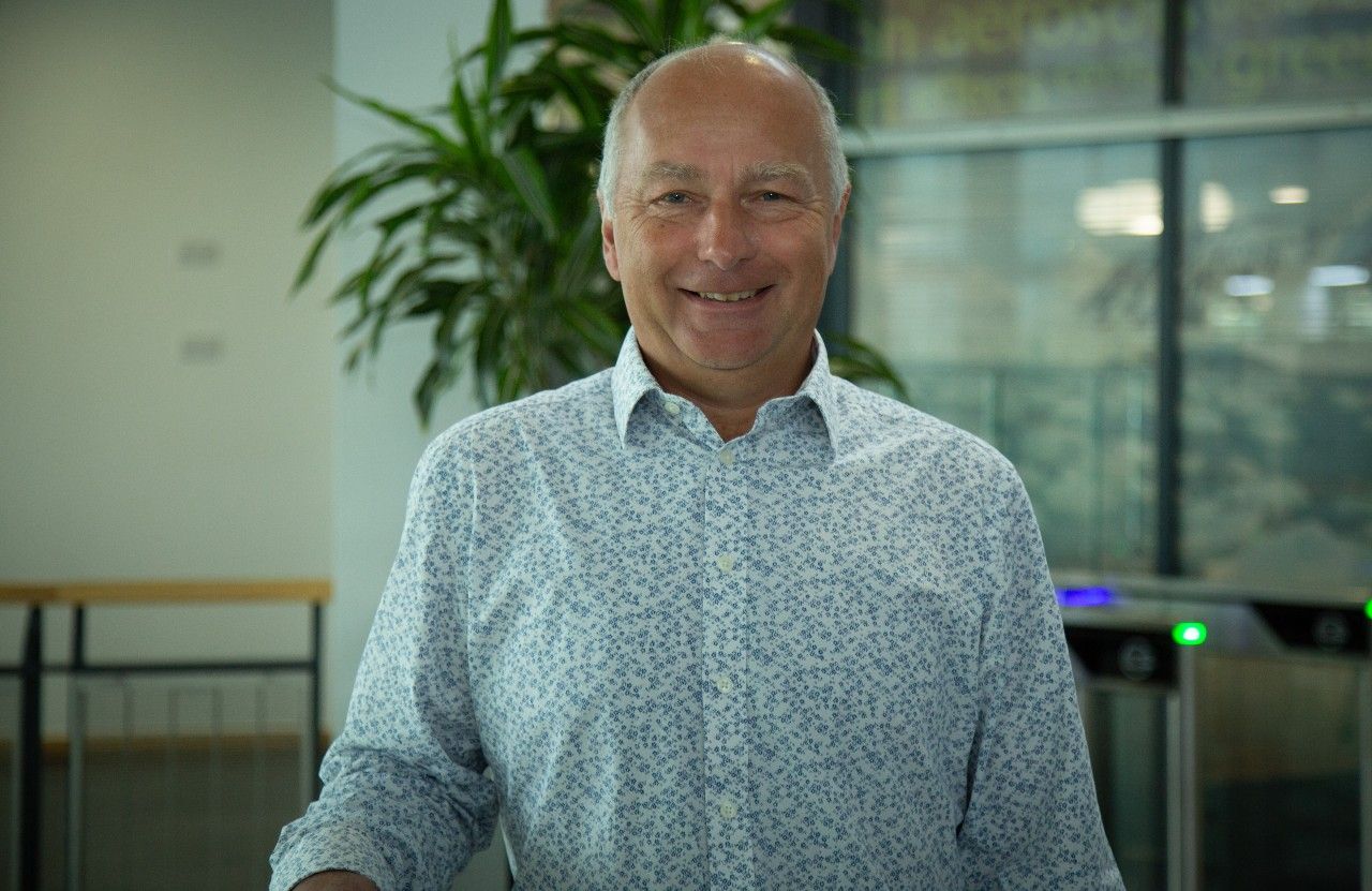 Professor Peter Stott MBE, Climate Science Fellow&nbsp;at the Met Office standing in the Met Office HQ for a portrait photo wearing a patterned shirt with a plant in the background.