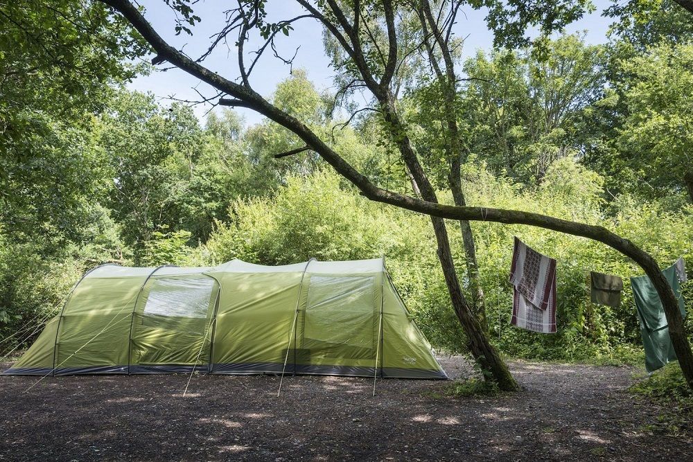 A large tent set up in the woodland, with some towels hanging to dry from a branch