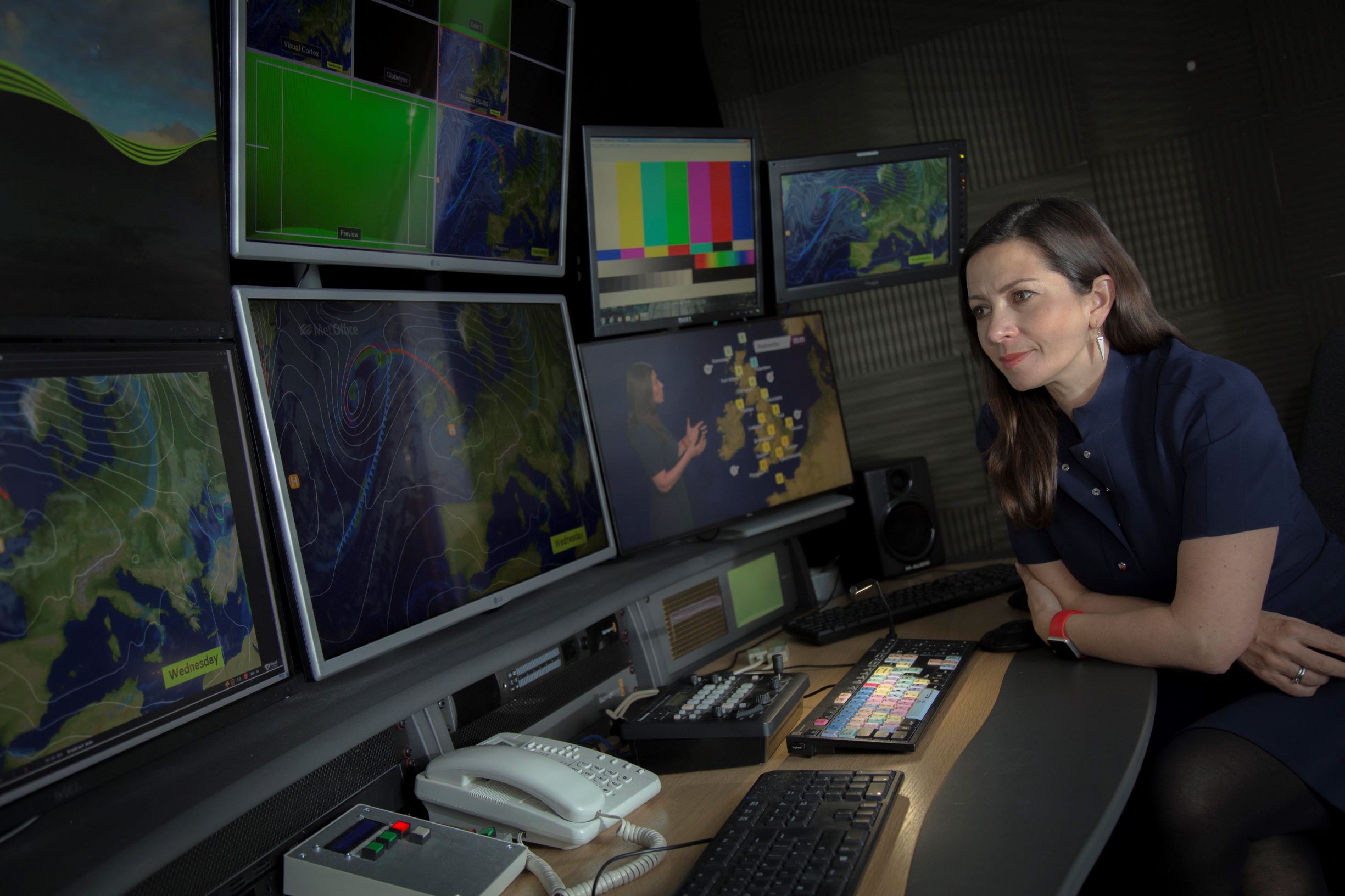 Clare Nasir looks at some monitors showing weather maps and a broadcast of the weather forecast.