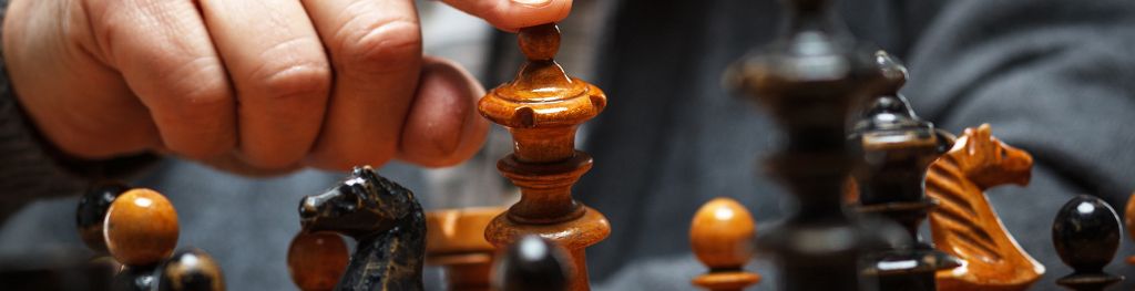 Close up image of chess pieces on chess board, with players finger on top of queen, starting to push piece over