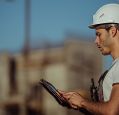 A construction worker wearing a hard out checks his iPad