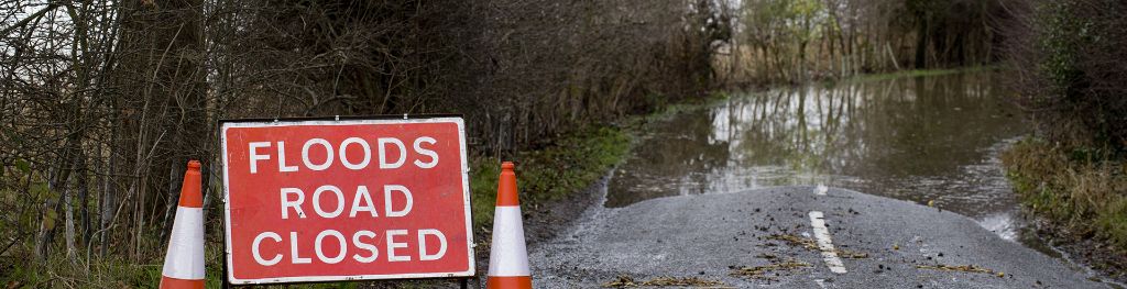 Two traffic cones and a road sign reading 'Floods road closed' in a flooded road