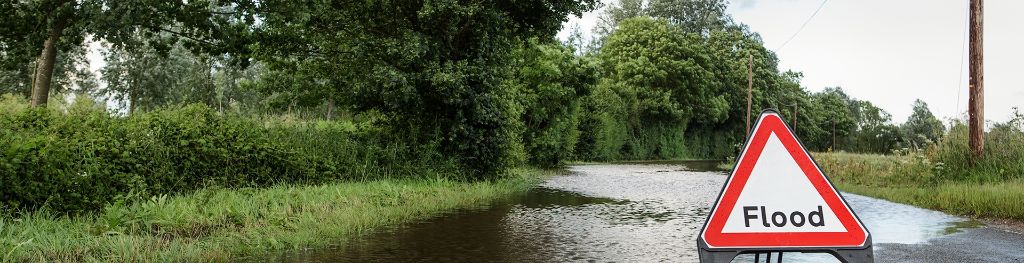 A flood warning sign in the middle of a closed, water-logged countryside road