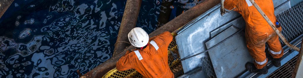 Two oil rig workers stand on the platform and look down at the sea