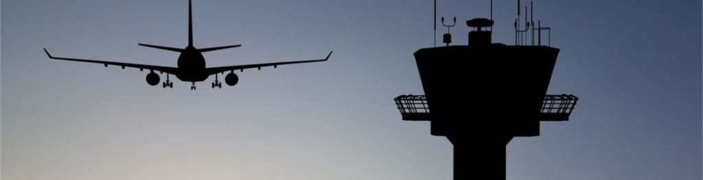 The silhouettes of a plane next to an airport tower at dawn.