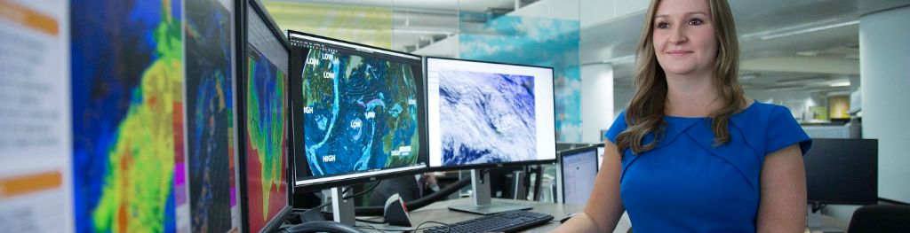 A Met Office meteorologist in front of her computer monitors displaying weather maps.