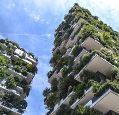 high apartment building in front of blue sky, with lots of green plants growing on balconies