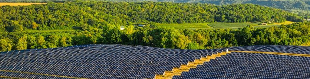 green landscape before blue sky with field of solar panels in the front