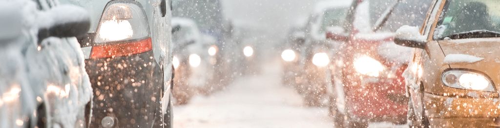 A view between two rows of traffic with headlights on, in the snow.