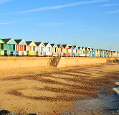 Beach huts on a promenade above sea defences, viewed from the shoreline with a pebble beach