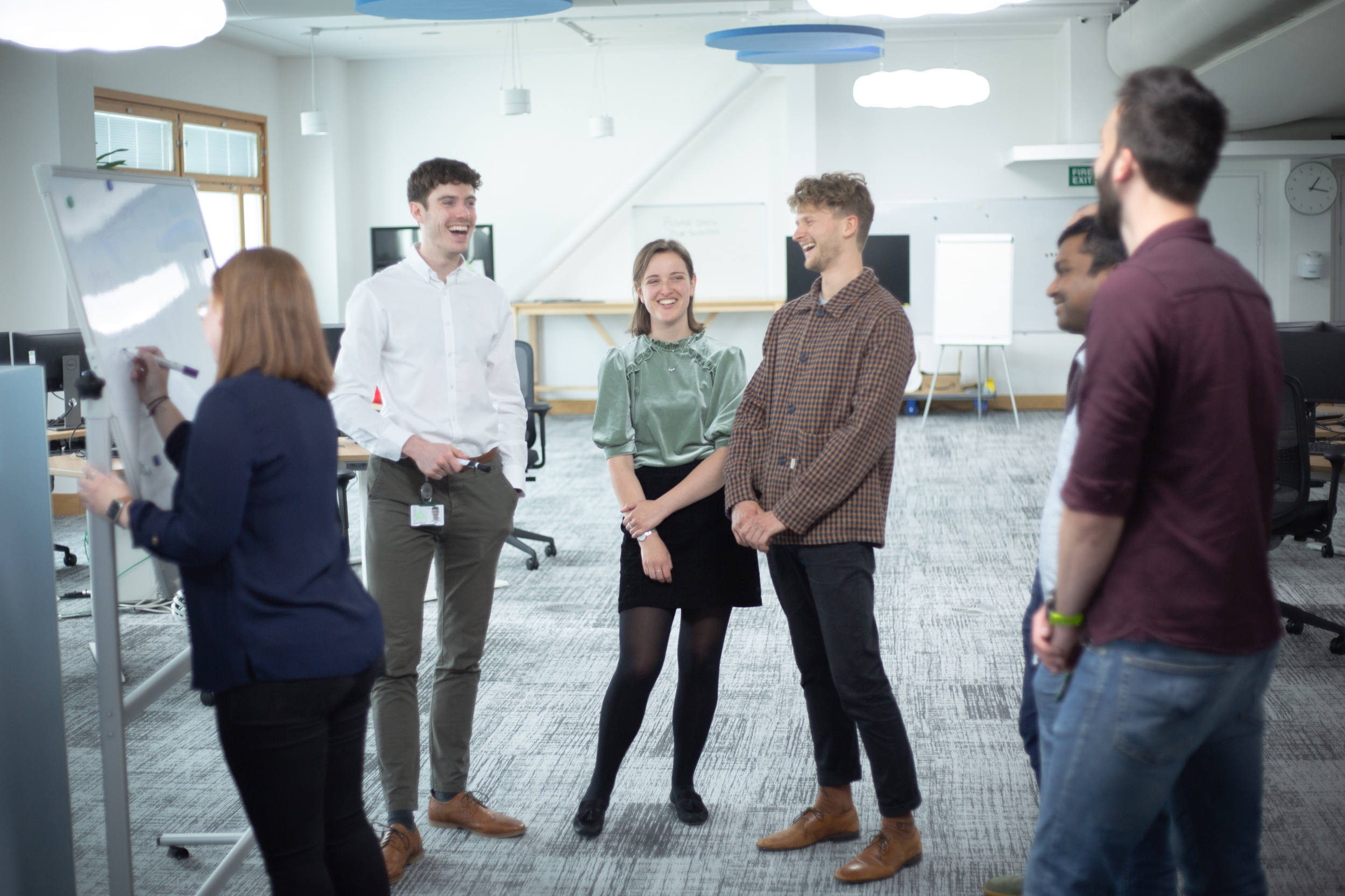 This photo shows a group of people in a room laughing together, except one person is writing on a whiteboard