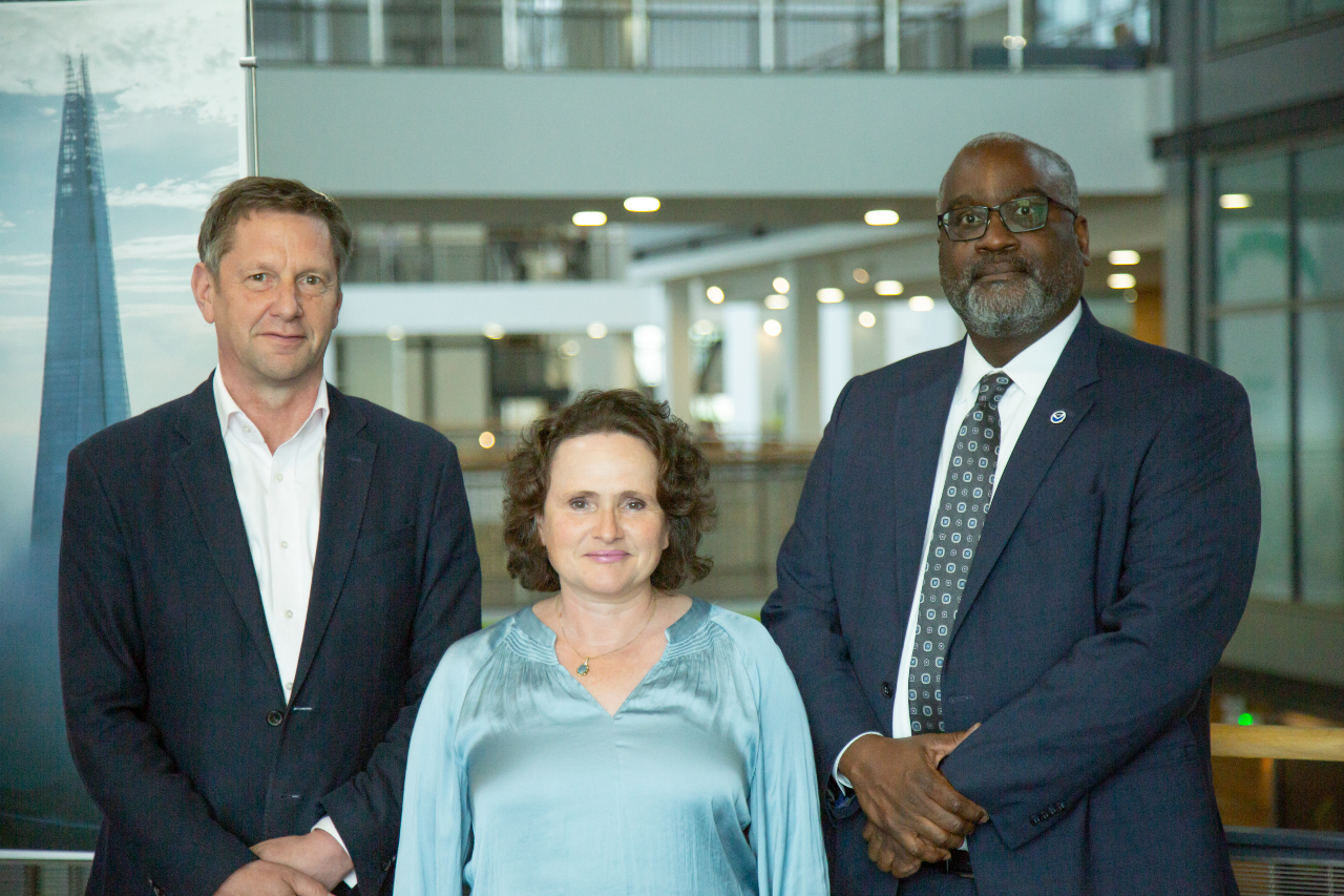 Prof Stephen Belcher wearing a white shirt and dark jacket with Prof Penny Endersby wearing a light blue top and Dr Michael Morgan wearing a dark suit, white shirt and tie all looking at the camera inside Met Office HQ.