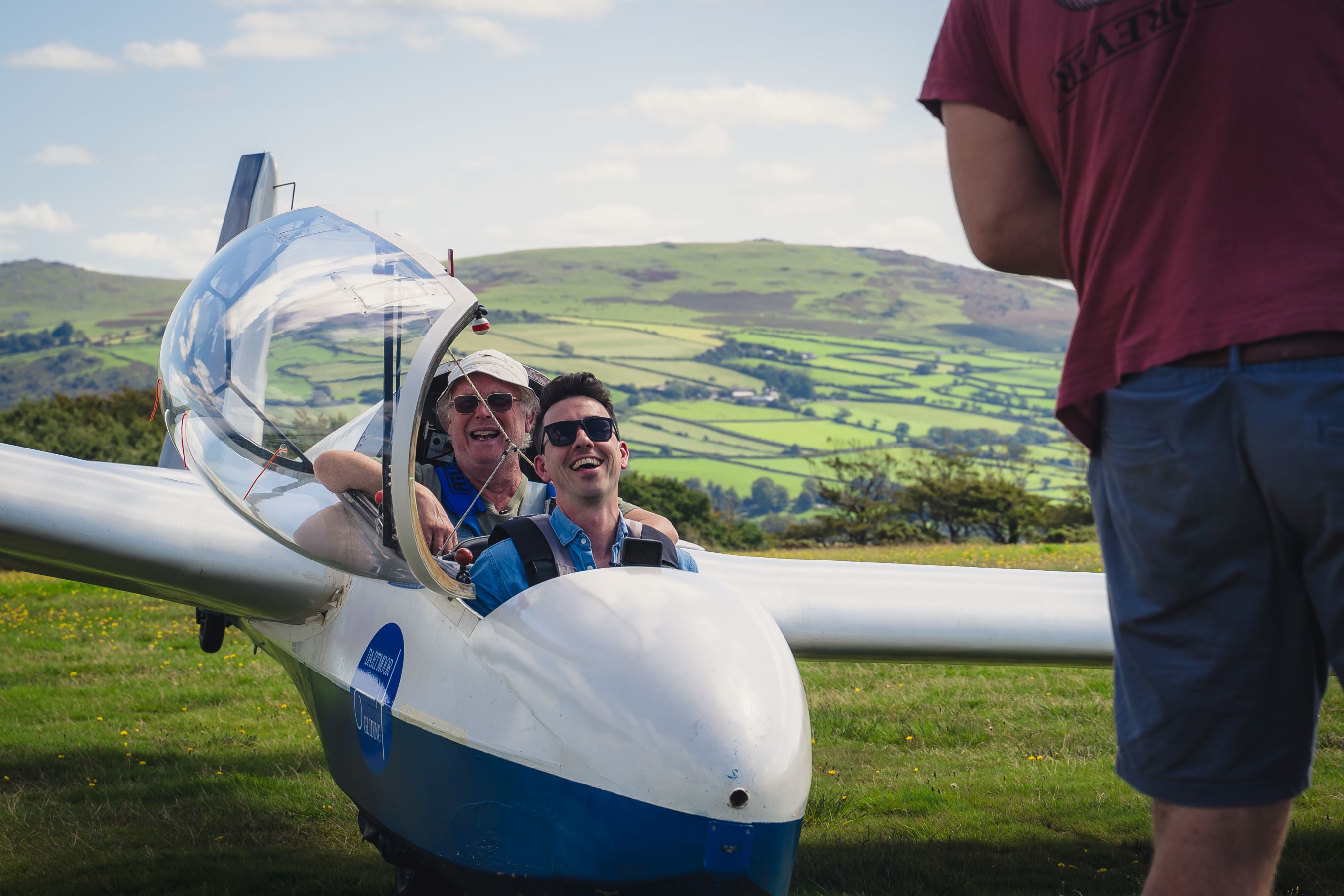 Two people laughing whilst sat in a grounded, white glider's cockpit