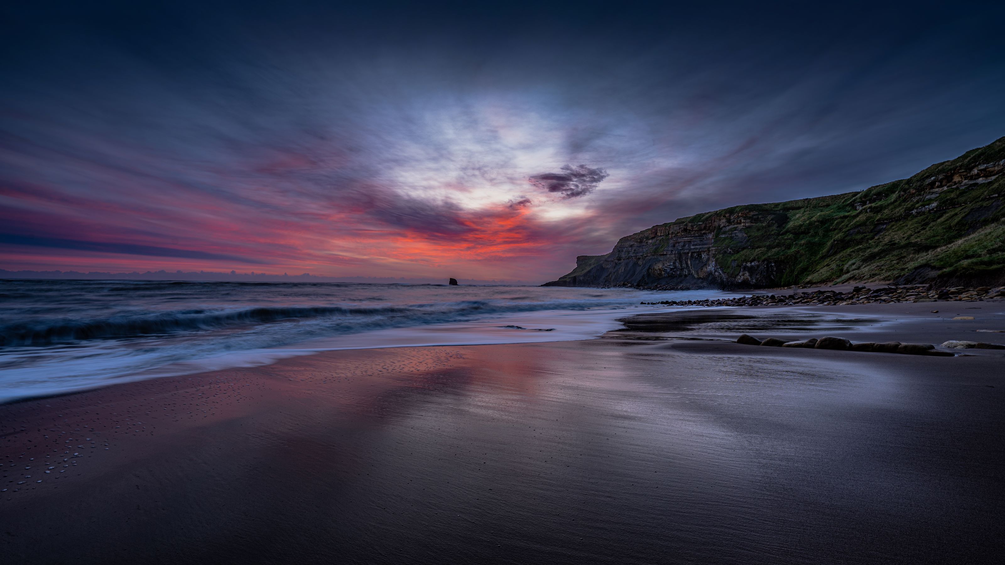 A landscape image of beach and sea being overlooked by rugged cliffs