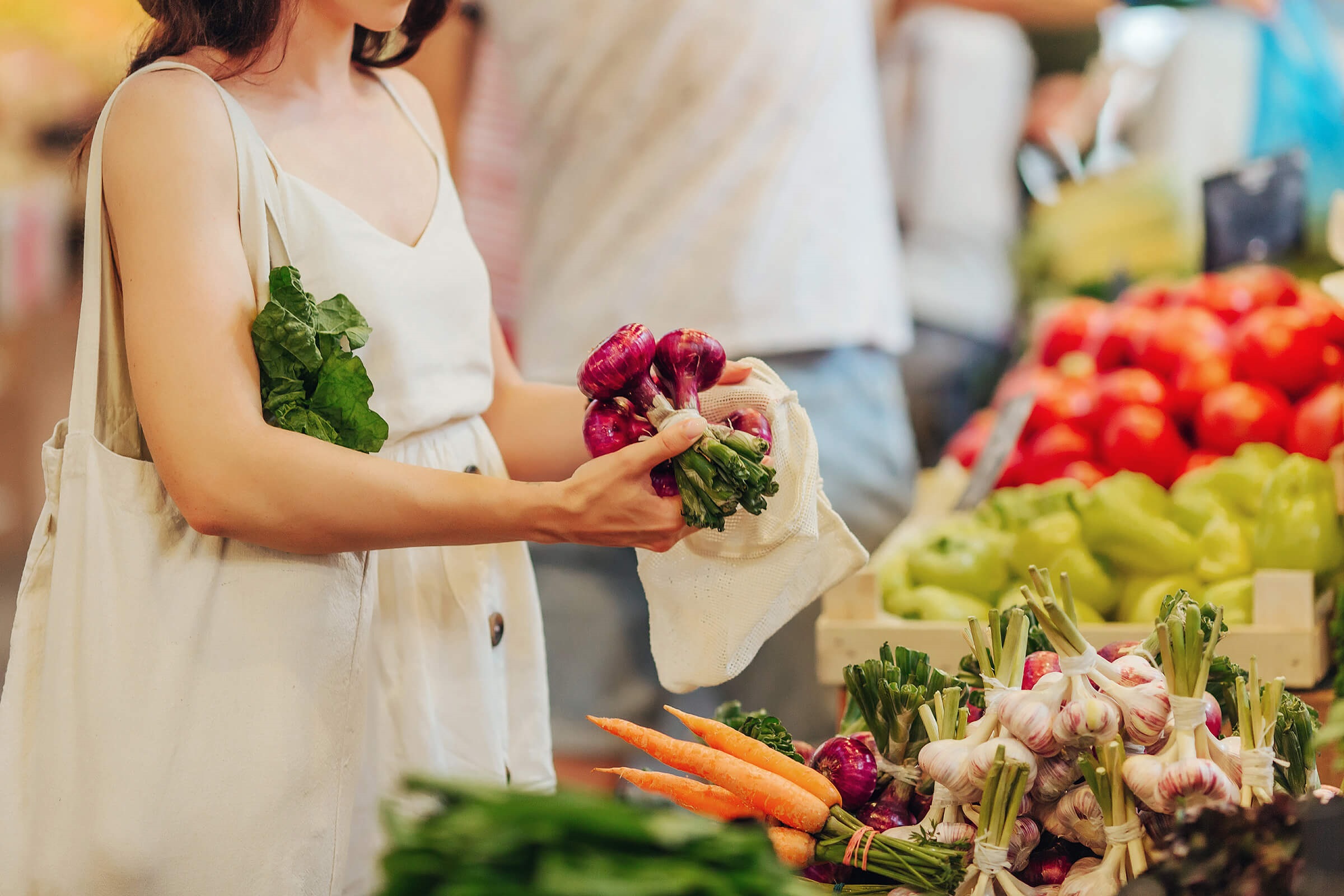 A woman in the supermarket by some vegetables holding a bunch of onions.