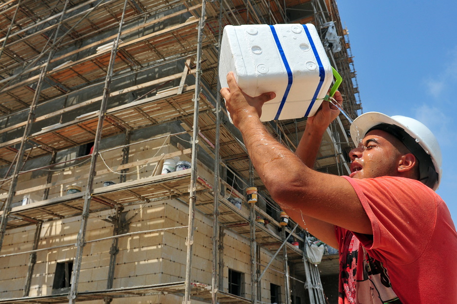 A construction worker pouring water over their face on a hot day.