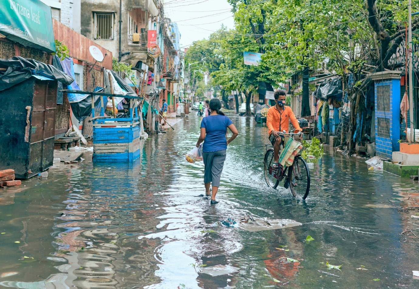 A photo of a person walking and a person cycling through a flooded street