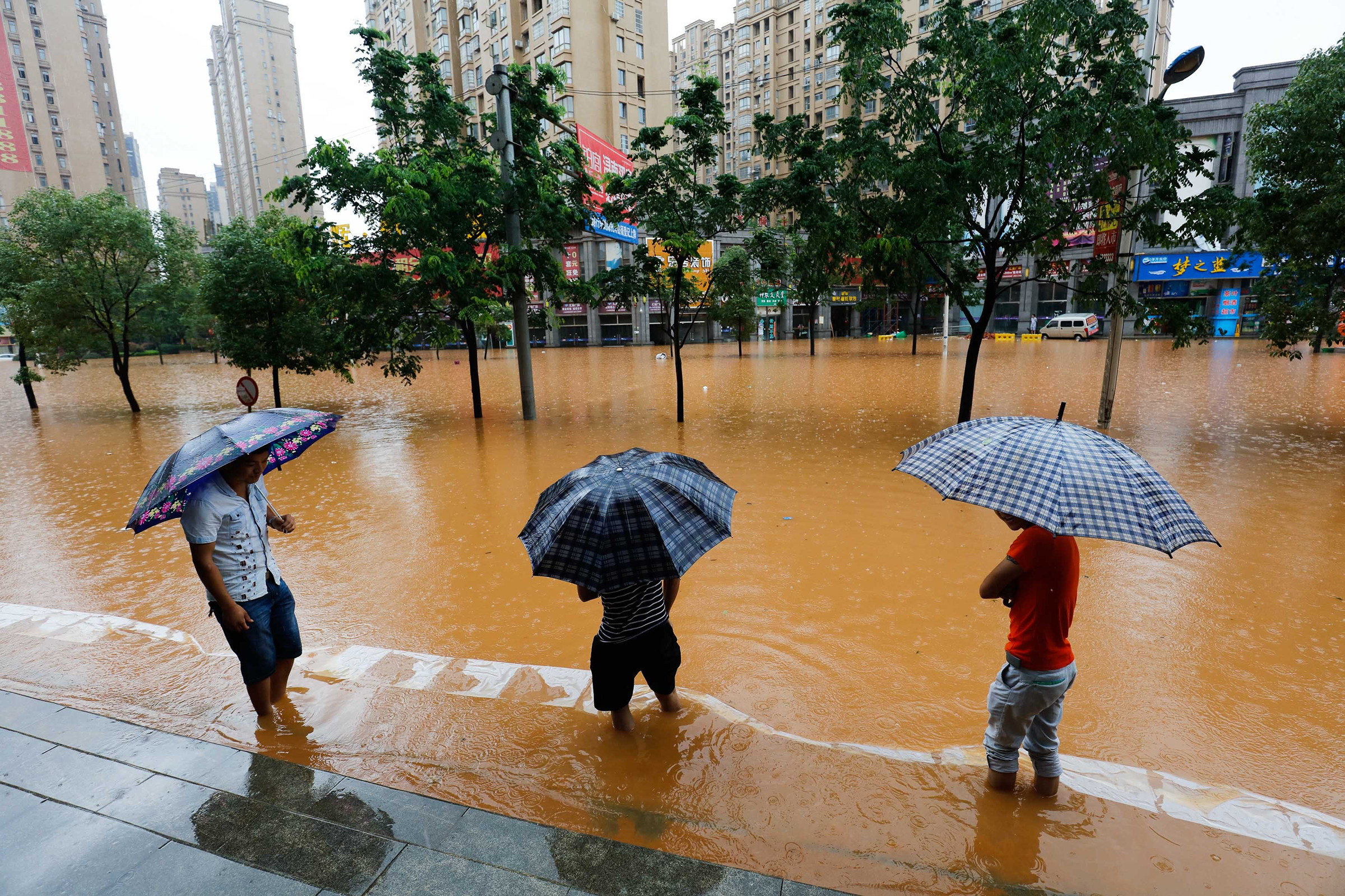 Decorative photo showing three people with umbrellas standing in a flooded street