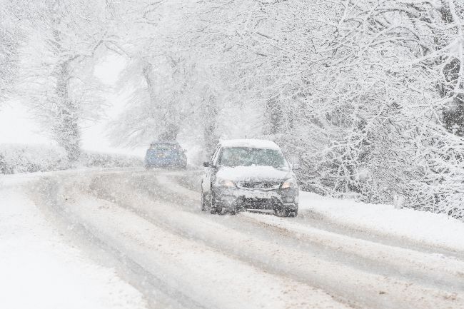 Car driving in heavy snow with snow lying on the road and in the trees around it.
